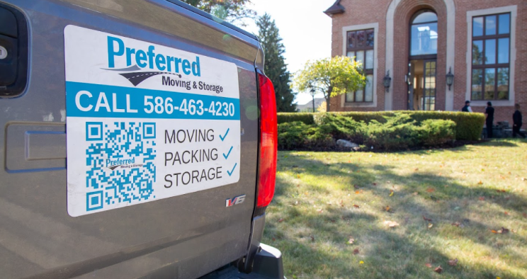 Close-up of a Preferred Moving & Storage truck with contact information and QR code, parked outside a residential home during a move.