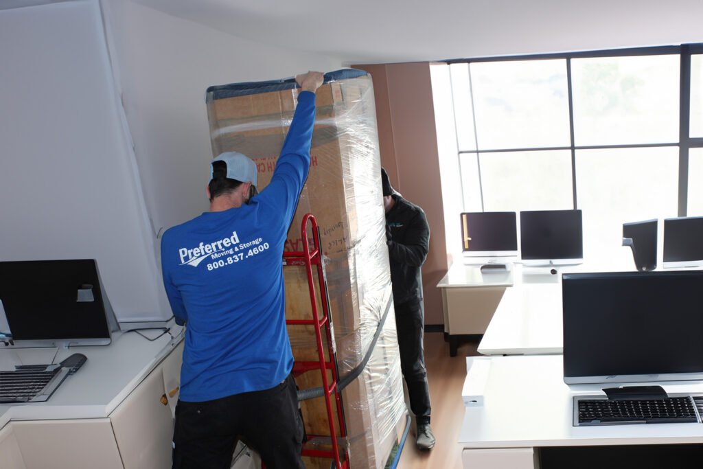 Alt Text (for provided image): Preferred Moving and Storage mover carefully maneuvering wrapped furniture on a hand truck through a tight indoor space